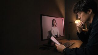 深夜の机で無音のインタビュー映像と写真メモを比較する30代男性